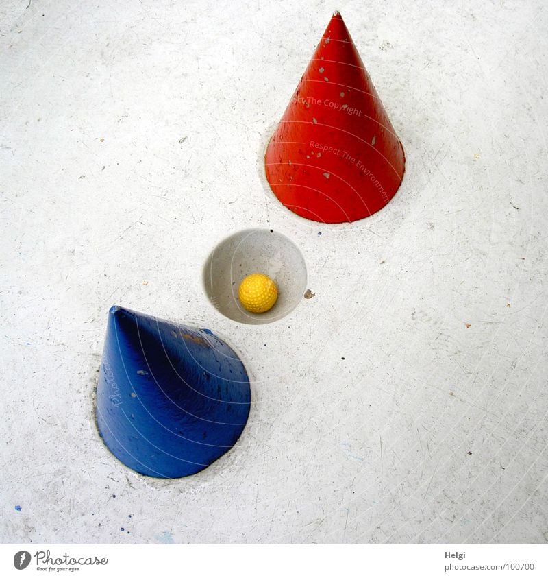 gelber Minigolfball liegt in einem Loch auf einer grauen Minigolfbahn mit rotem und blauem Kegel Golfball schwierig zielen schlagen Sportveranstaltung Spielen