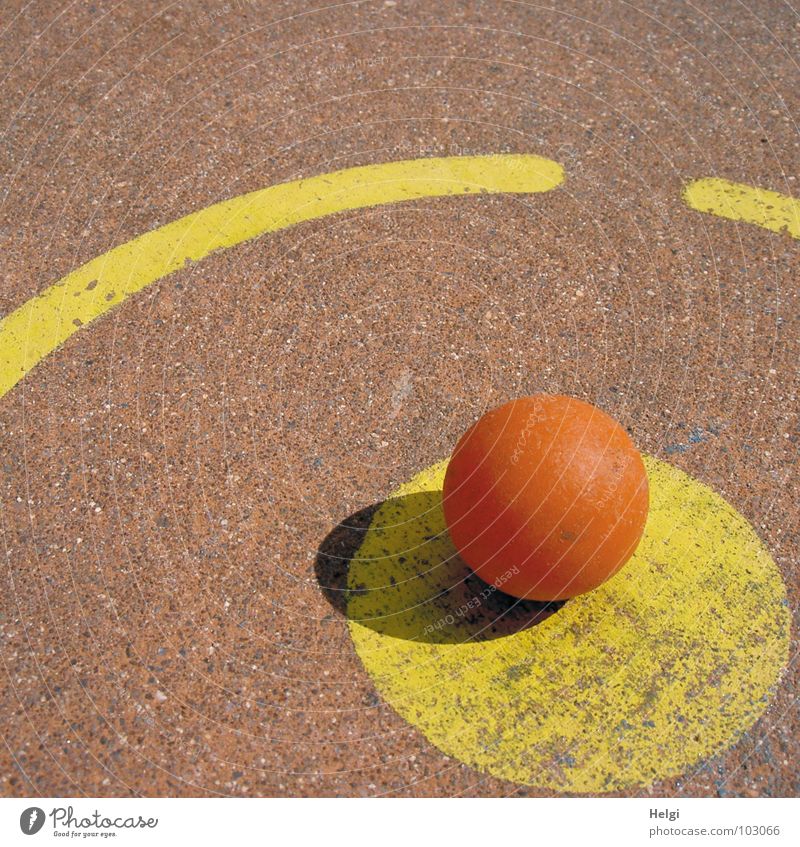orangefarbiger Minigolfball liegt am Abschlagpunkt auf einer Minigolfbahn rund schlagen Spielen Sportveranstaltung gelb rot Beton angemalt verlieren