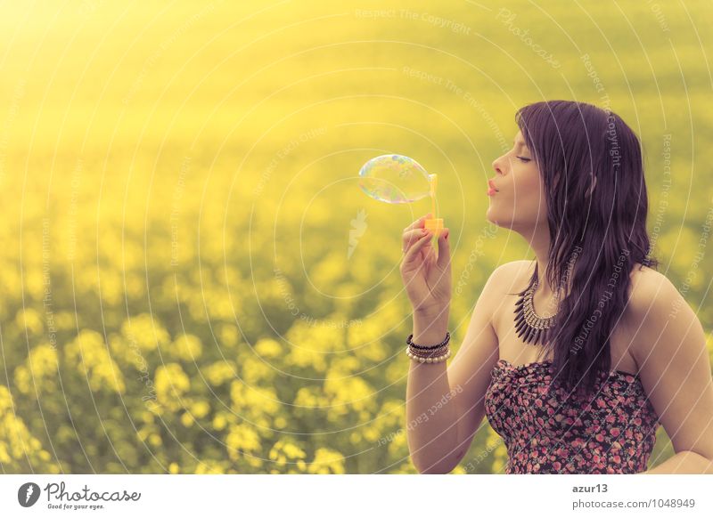 Schöne junge Frau mit Seifenblase im Sommer auf gelber Wiese aus Raps bis zum Horizont. Hübsches Mädchen mit Lebensfreude geniesst die Sonnenschein Pause und das Leben. Erholung und Energie tanken vom Zeit Stress in der Umwelt und Natur Idylle.