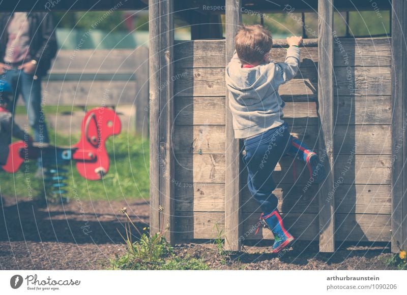 Kind mit bunten Gummisteifel klettert auf Holzhaus am Spielplatz Freizeit & Hobby Spielen Garten Spielturm Kindergarten Mensch maskulin Mann Erwachsene Vater