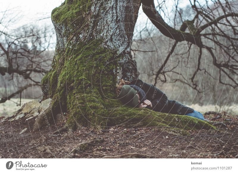 Frau liegt zusammengekauert unter einem Baum mit dicken Wurzeln Mensch Erwachsene Leben Körper Hand 1 Erde Frühling Moos Baumrinde Mantel Schal Mütze
