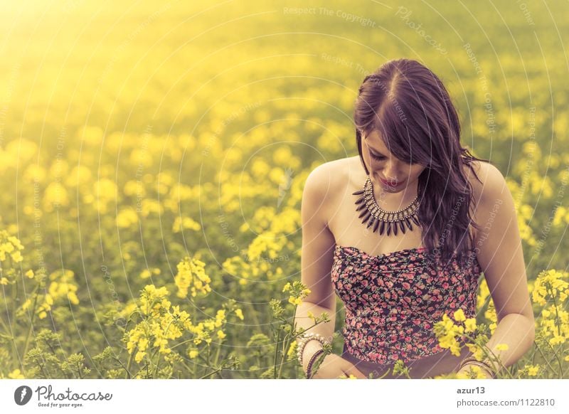 Nachdenkliche junge Frau mit gesenktem Kopf auf gelber Wiese. Attraktives Mädchen mit geneigtem Haupt auf einer Wiese aus Blumen in gelb bis zum Horizont im Sonnenschein im Frühling oder Sommer. Foto einer Serie.