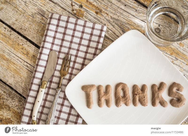 Die Buchstaben THANKS  auf einem Teller mit Serviette, Messer und Gabel und Wasserglas auf einem rustikalen Holztisch Ernährung Fastfood Fingerfood