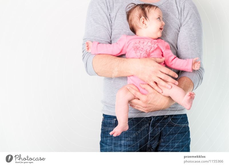 Vater hält seine lächelnde Tochter. Das Baby trägt einen rosa Anzug und schaut auf die rechte Seite. Lifestyle schön Leben Kindererziehung Mädchen Mann