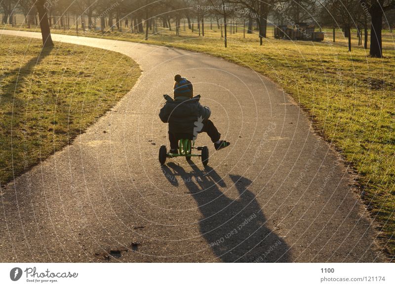 Der Sonne entgegen Dreirad Fahrer Kind Abendsonne Sonnenuntergang Fahrzeug Verkehrsmittel Schuhe Muskulatur Junge Straße Wege & Pfade Baumwiese Bübchen Schatten