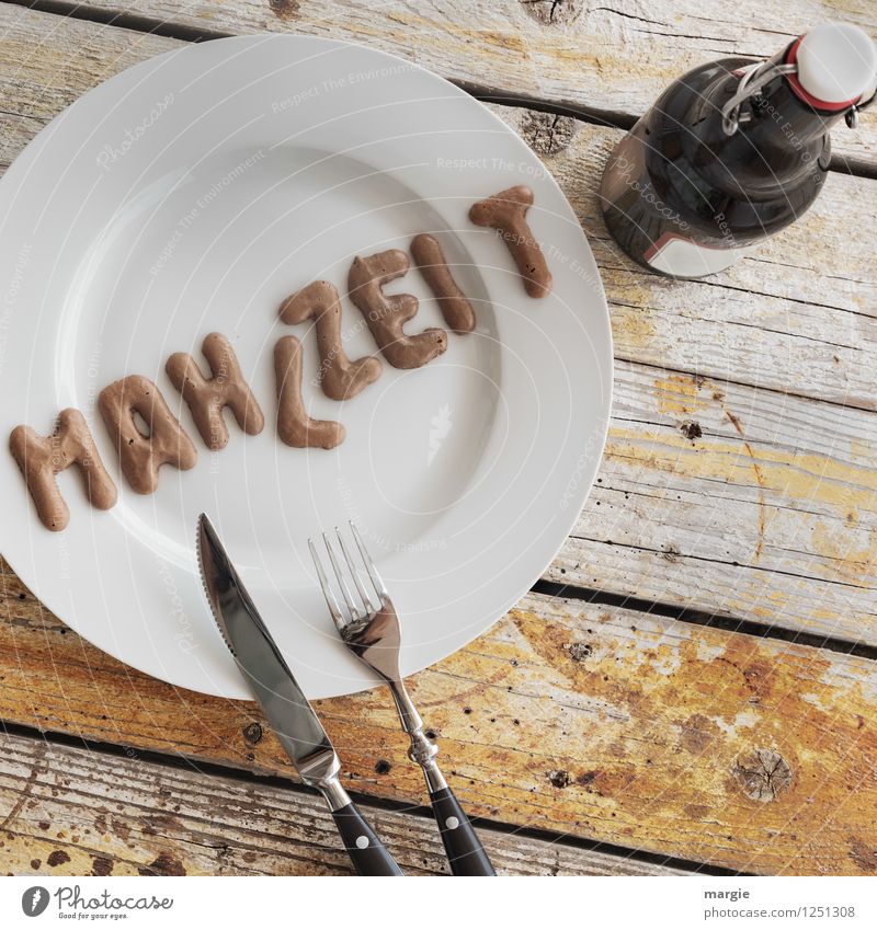 Auf einem rustikalen Holztisch ein Teller mit den Buchstaben MAHLZEIT, Messer und Gabel und eine Flasche Bier Lebensmittel Ernährung Mittagessen Abendessen