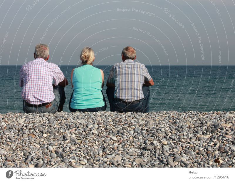 Rückansicht  einer Seniorin und zwei Senioren, die auf Kies sitzen und aufs Meer schauen Ferien & Urlaub & Reisen Mensch maskulin feminin Frau Erwachsene Mann