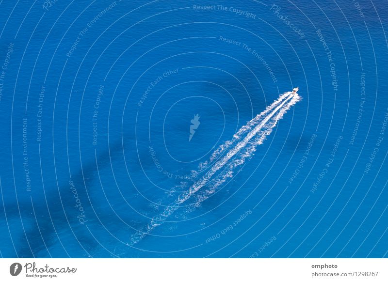 Luftaufnahme eines Motorbootes, das in einem türkisblauen Meerwasser schwimmt. Das Boot bewegt sich diagonal durch den Rahmen des Fotos.