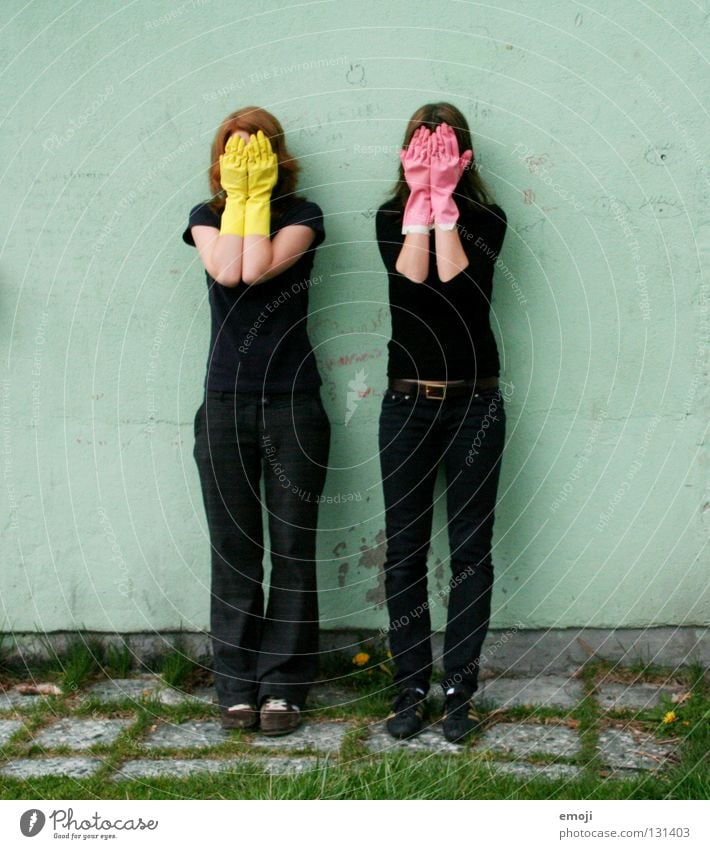 zwei Frauen verstecken sich hinter Gummihandschuhen Handschuhe rosa gelb knallig Rauschmittel türkis Wand beschrieben dreckig Reinigen edel skurril seltsam