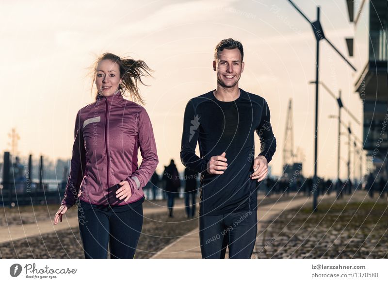 Aktives junges Paar joggt Seite an Seite in einer städtischen Straße Lifestyle Glück Gesicht Sport Erfolg Joggen Frau Erwachsene Mann 2 Mensch 18-30 Jahre