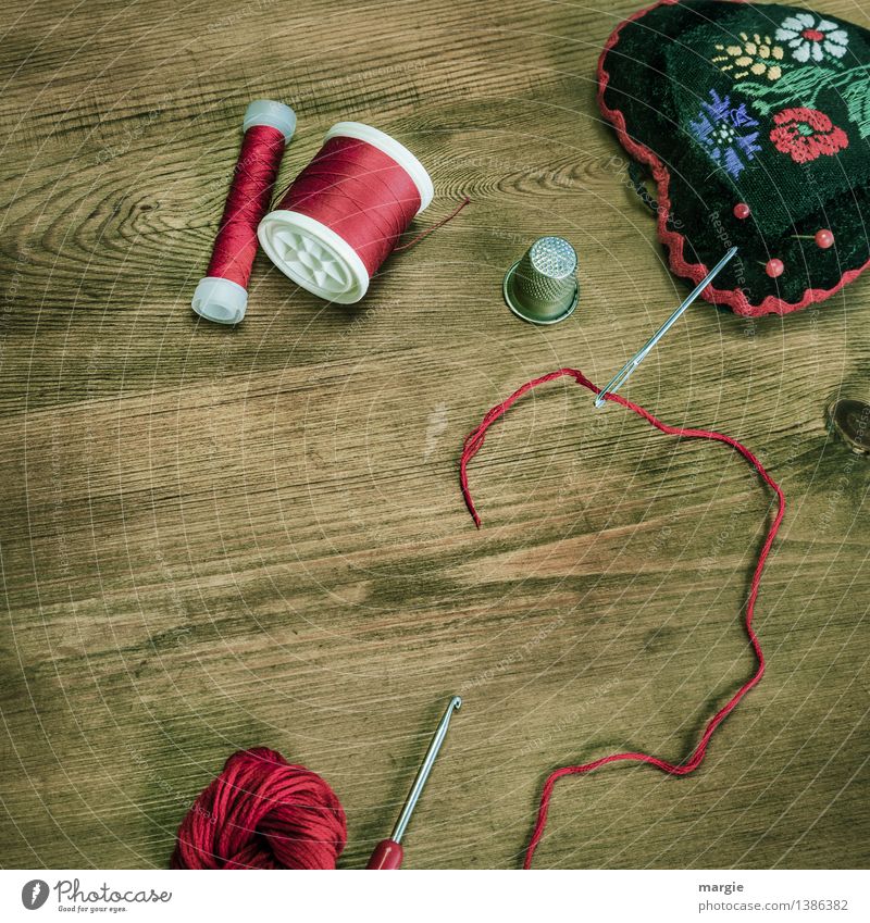 Rot eingefädelt: Nähzeug, wie Nadel, Garn, Fingerhut Wolle, Häkelnadel und ein Nadelkissen auf einem Holztisch Freizeit & Hobby Handarbeit stricken