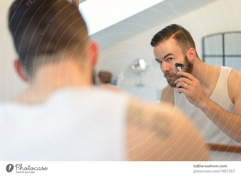 Junger Mann, der über seinem Bart sich rasiert Gesicht Spiegel Bad Erwachsene Vollbart Sauberkeit Präzision Vorschein Pflege Kaukasier Wange konzentrierend