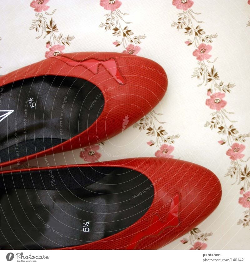 Rote Schuhe mit einer Blitz applikation liegen auf einer geblümten Tapete. Ausgehen, Diskothek, tanzen. Retro ausgehen Mode Bekleidung Leder Damenschuhe Kitsch