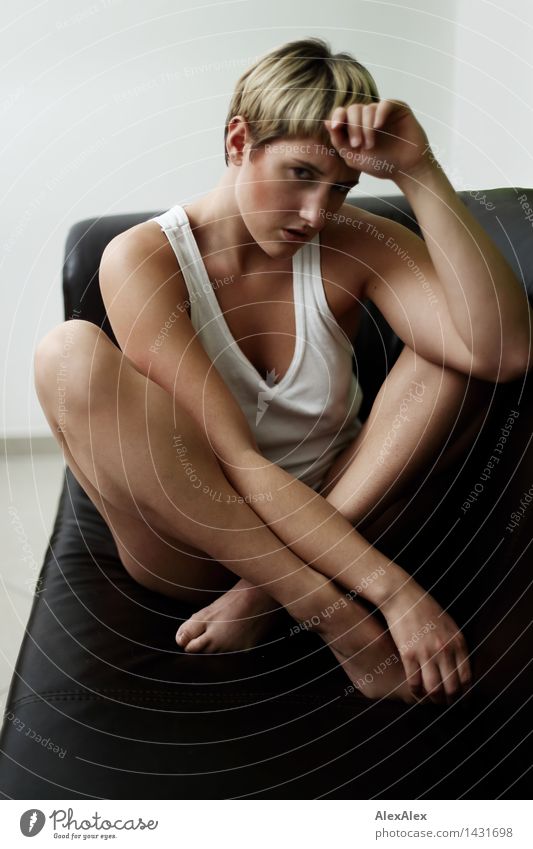 Junge, sportliche, schlanke Frau sitzt barfuß in Unterwäsche auf dunkler Couch im Schneidersitz Sofa Junge Frau Jugendliche Gesicht Beine 18-30 Jahre Erwachsene