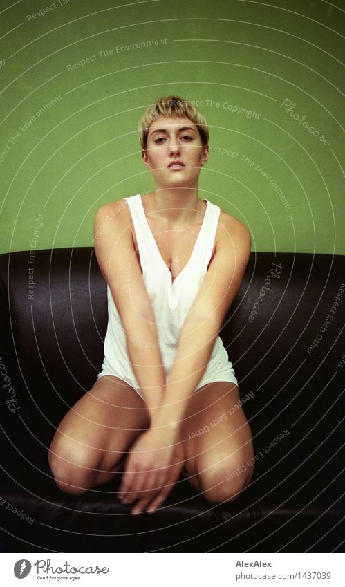 Analoges Portrait (35mm) einer jungen, schlanken, sportlichen Frau, die in Unterwäsche auf einer Couch sitzt und in die Kamera schaut Erholung ruhig Junge Frau