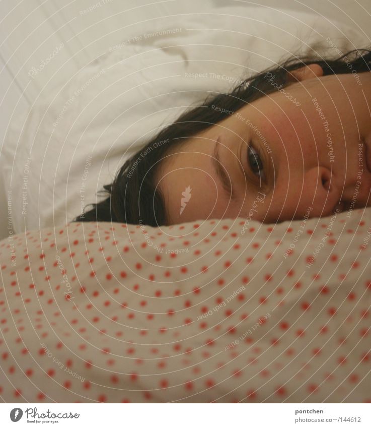 Frau liegt im Bett auf einem gepunkteten    Kopfkissen und schaut   traurig. Müdigkeit, Depression, Krankheit, burn out Gesicht Erholung Schlafzimmer feminin