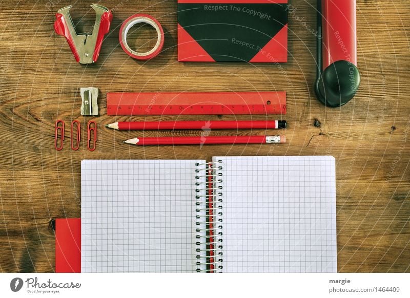 Querformat: Rot- schwarze Schreibtisch Utensilien auf einem Holztisch. Heft, Bleistifte, Lineal, Klebeband, Spitzer, Büroklammern, Buch, Hefter, Klammeraffe