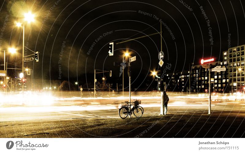 Mann steht neben Fahrrad nachts an Berliner Straßenkreuzung mit Verkehr Stadt Verkehrswege Wegkreuzung Ampel PKW Bewegung Geschwindigkeit Nachtaufnahme KFZ