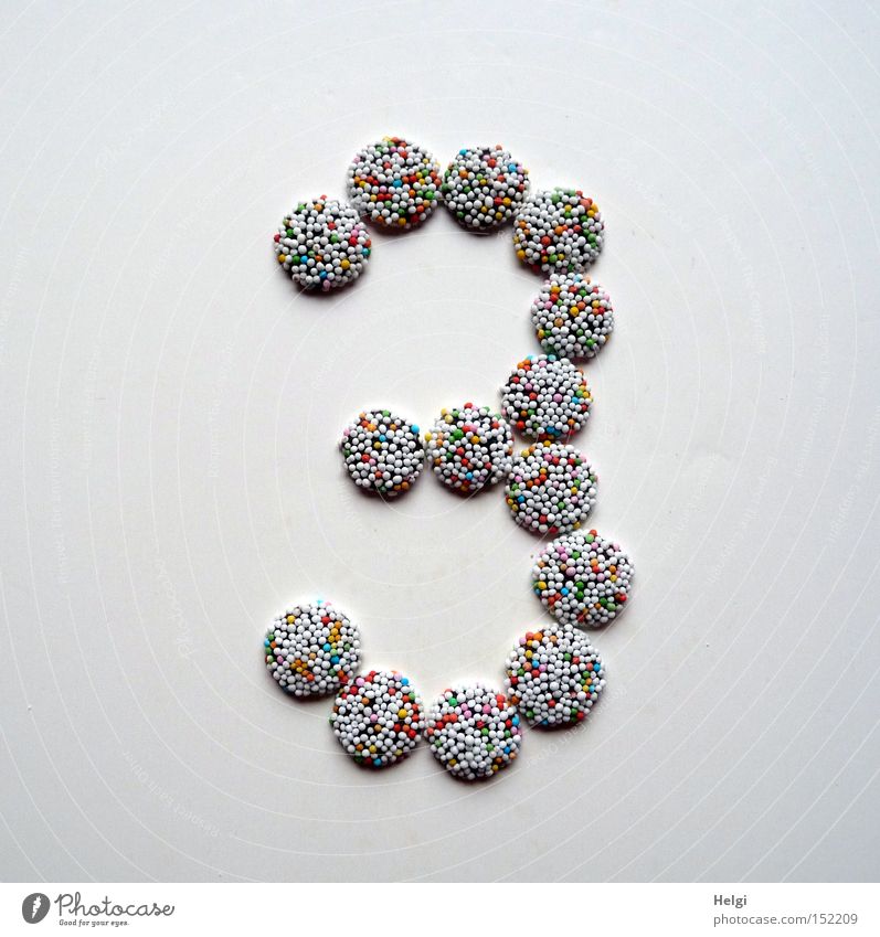 Zahl 3 gelegt aus kleinen Schokoladenbonbons mit bunten Zuckerstreuseln auf weißem Hintergrund Ziffern & Zahlen Adventskalender Bonbon Süßwaren Streusel