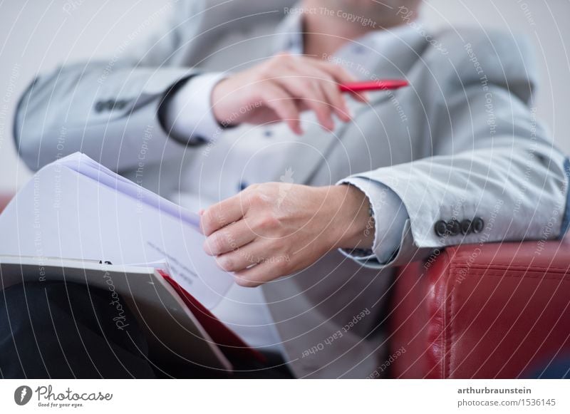 Geschäftsmann im Anzug mit Unterlagen in der Hand auf roter Couch Berufsausbildung Studium lernen Büroarbeit Arbeitsplatz Wirtschaft Dienstleistungsgewerbe