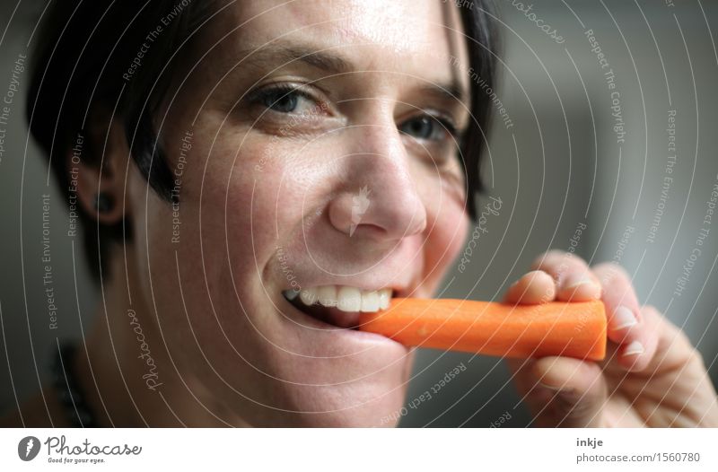 Lächelnde Frau isst Karotte Gemüse Möhre Ernährung Essen Bioprodukte Vegetarische Ernährung Fingerfood Gesundheit Gesunde Ernährung Erwachsene Leben Gesicht 1