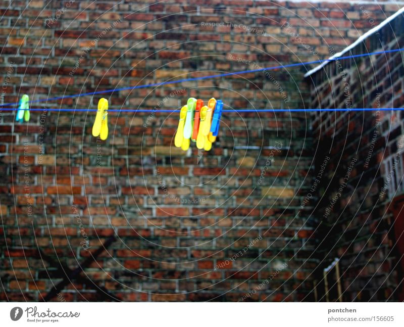 Bunte Wäscheklammern hängen an einer Wäscheleine in einem Hinterhof. Haushalt Hof Backstein Mauer trist leer trocknen aufhängen Deutschland Haushaltsware