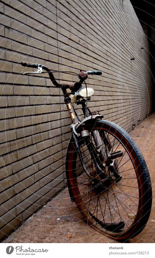 Ein altes Fahrrad mit platten Reifen lehnt an einer Klinkerwand in einer Fabrikhalle. ruhig Rost Backstein kaputt Einsamkeit Vergangenheit Vergänglichkeit