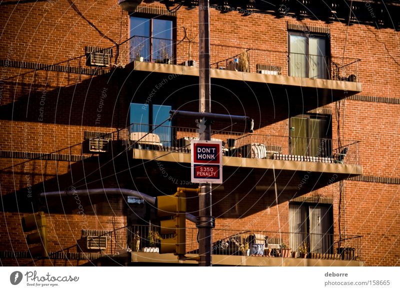 Strafzeichen "Hupen Sie nicht" auf einem Laternenpfahl vor einem New Yorker Wohnhaus aus rotem Backstein mit Balkonen. Wohnung Haus Fenster