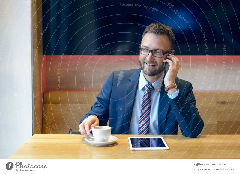 Gutaussehender Geschäftsmann mit gestreifter Krawatte sitzt am Tisch mit Kaffee, telefoniert und benutzt sein Tablet Arbeit & Erwerbstätigkeit Business Telefon