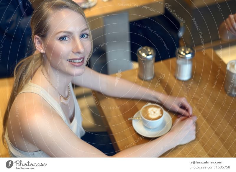 Lächelnde blonde Frau, die in einer Bar mit einem Cappuccino sitzt Kaffee Lifestyle schön Erholung Tisch feminin Erwachsene 1 Mensch 18-30 Jahre Jugendliche