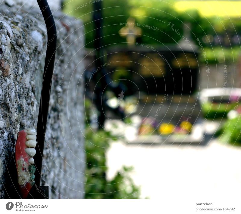 Ein verlorenes Gebiss befestigt an einem Kabel an einer Mauer am friedhof. Fundstück. Altern, Tod. Makaber  Grabsteine Und Kreuze im Hintergrund Trauerfeier