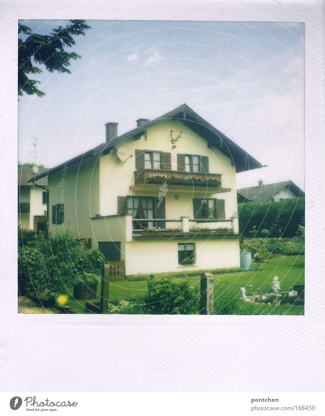 Ein typisch bayerisches Einfamilienhaus mit Balkonen und einem Hirschgeweih. Häuser im Hintergrund und Garten im Vordergrund. Siedlung in einer ländlichen Gegend. Nachbarschaft