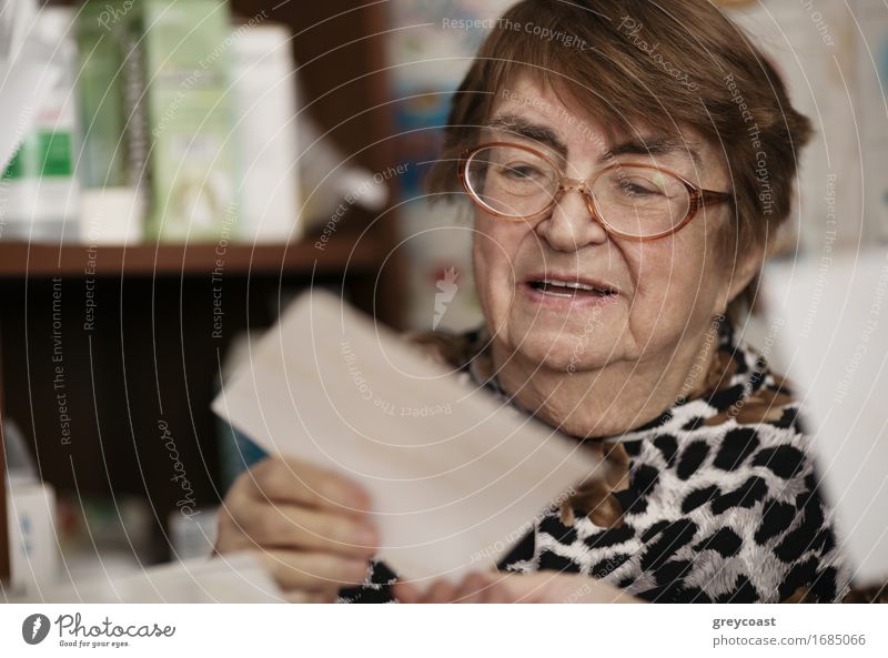 Ältere Frau mit Brille sitzt in ihrem Wohnzimmer und liest einen Brief, Nahaufnahme Porträt Lifestyle Gesicht lesen Lehrer Ruhestand Mensch Erwachsene