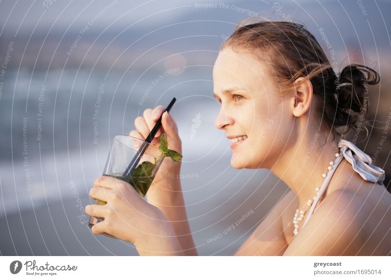 Schöne junge Frau genießt einen Abend Cocktail sitzen mit Blick auf einen tropischen Strand mit ihrem Gesicht in Richtung der untergehenden Sonne gedreht
