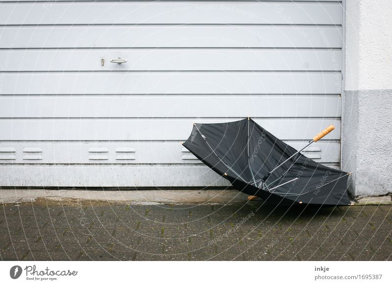 schwarzsehen | deutscher Sommer Wetter schlechtes Wetter Wind Sturm Regen Menschenleer Mauer Wand Fassade Garagentor Regenschirm trist grau kaputt fliegen