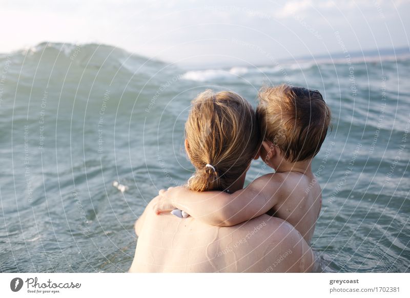 Mutter schwimmt im Meer mit ihrem kleinen Sohn im Arm und beobachtet eine entgegenkommende Welle, Blick von hinten Erholung Ferien & Urlaub & Reisen Sommer Kind
