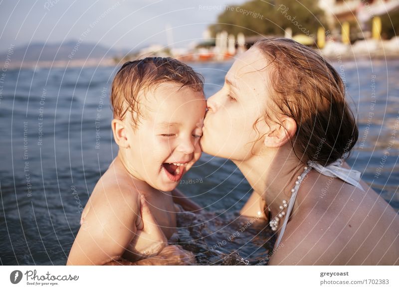 Mutter küsst ihr kleines Kind beim Baden im Meerwasser während des Sonnenuntergangs Spielen Ferien & Urlaub & Reisen Strand Wellen Mensch Junge Junge Frau