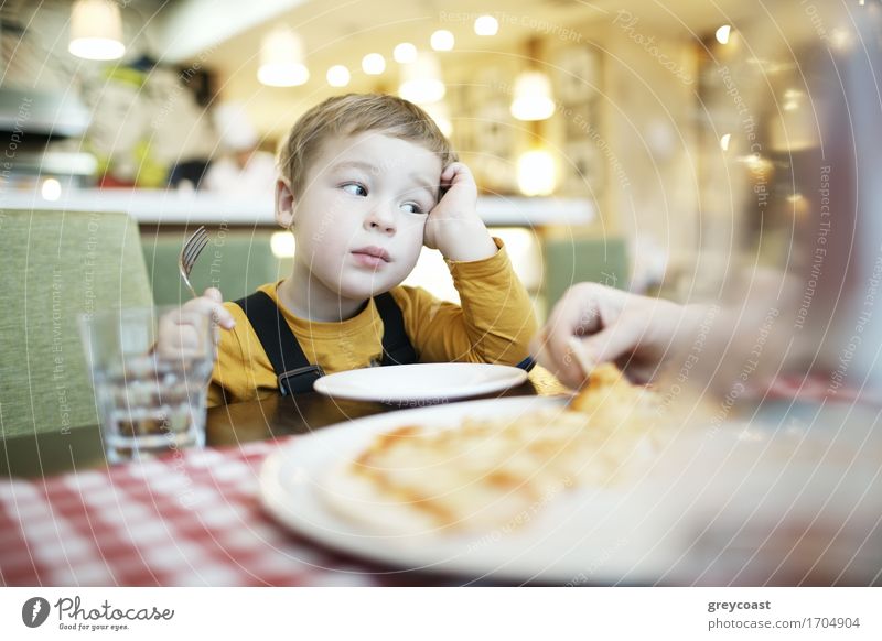 Gelangweilter kleiner Junge in einem Restaurant mit einem leeren Teller vor sich sitzend und den Kopf auf seine Hand gestützt Ernährung Essen Mittagessen