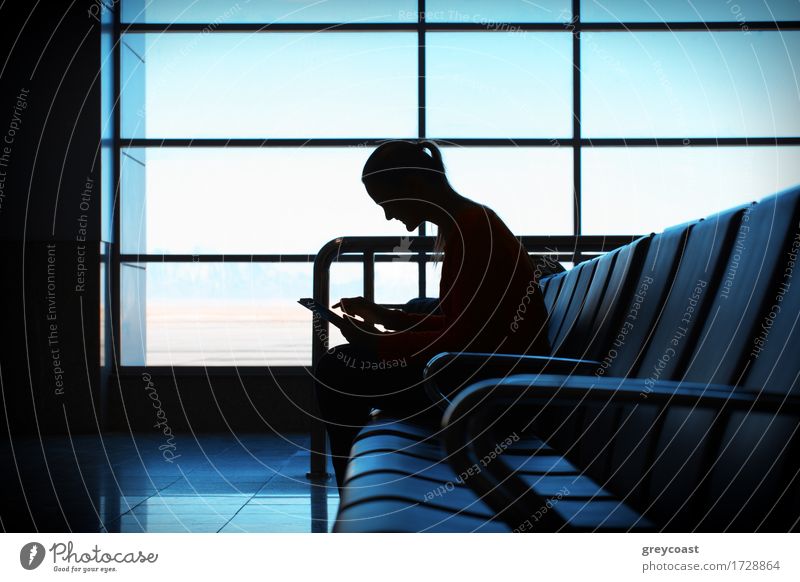 Frau in der Flughafen-Lounge sitzt im Stuhl am Fenster und verwendet einen Tablet-Computer für die Überprüfung ihrer Flugdaten mit WiFi-Verbindung. Silhouette