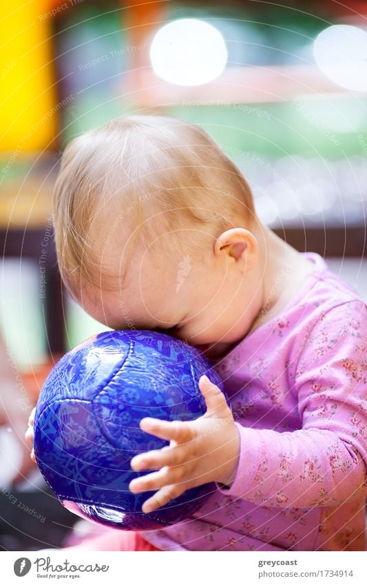 Nettes kleines Baby, das mit einem großen blauen Ball spielt, der mit seinem Gesicht gegen den Ball gedrückt wird, Seitenansicht Freude Spielen Sommer Kind