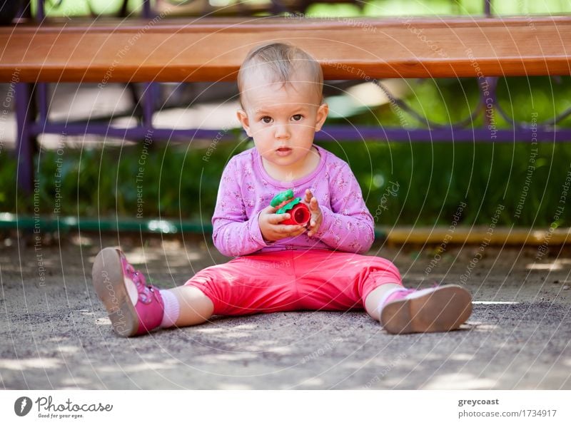 Kleines Baby spielt mit Spielzeug sitzt auf dem Boden im Park und schaut in die Kamera Freude Spielen Sommer Kind Mädchen Kindheit 1 Mensch 1-3 Jahre Kleinkind