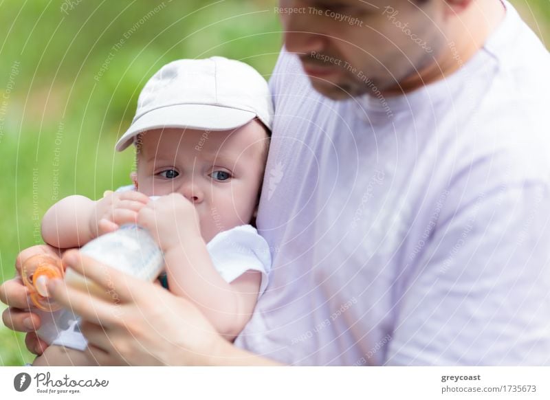 Fürsorglicher Vater füttert seinen kleinen Sohn aus der Flasche im Park Abendessen melken Garten Kind Baby Junge Junger Mann Jugendliche Eltern Erwachsene