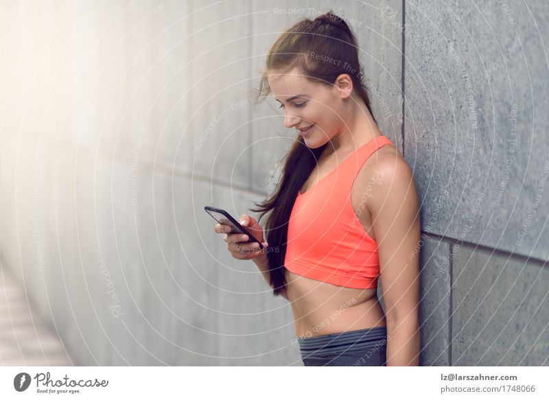 Sportliche junge Frau, die ihr Mobile überprüft Gesicht Sommer Telefon PDA Erwachsene 1 Mensch 18-30 Jahre Jugendliche Wärme brünett Fitness Lächeln stehen