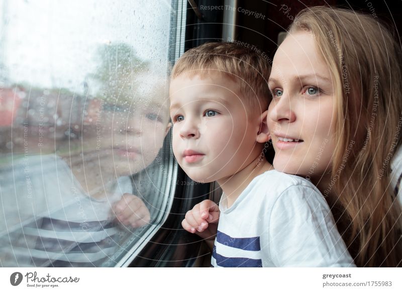 Mutter und Sohn schauen durch ein Zugfenster, während sie eine Tagesreise genießen, wobei sich das Gesicht des kleinen Jungen im Glas spiegelt