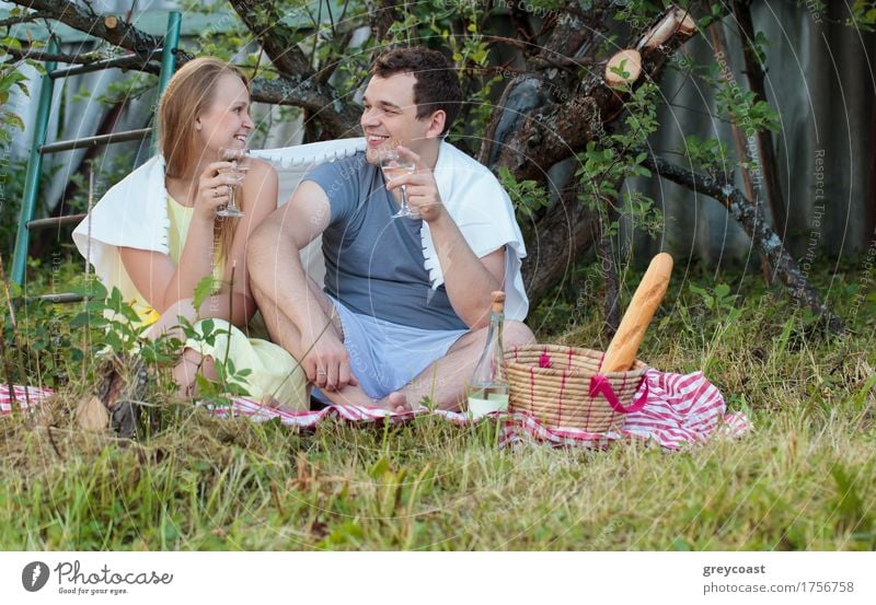Glückliches junges Paar beim Picknick auf dem Land. Sie sitzen auf dem Gras mit Gläsern von Wein mit Decke bedeckt. Romantische Momente zusammen Getränk Alkohol