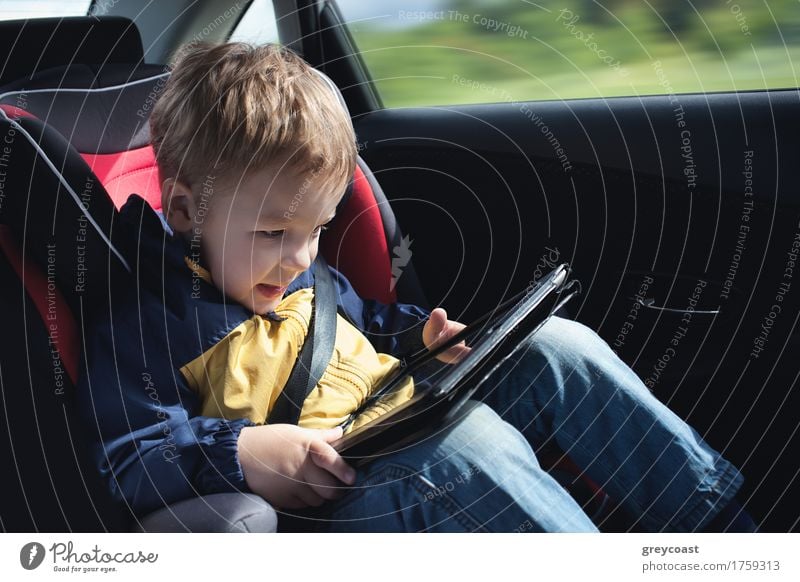 Aufgeregter kleiner Junge im Auto, der im Kindersitz sitzend mit dem Touchpad spielt Freude Glück Spielen Ferien & Urlaub & Reisen Ausflug Computer 1 Mensch