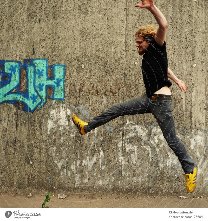 Junger Mann springt vor einer Betonwand Farbfoto Außenaufnahme Textfreiraum links Hintergrund neutral Tag Ganzkörperaufnahme Profil Blick nach vorn Stil Freude