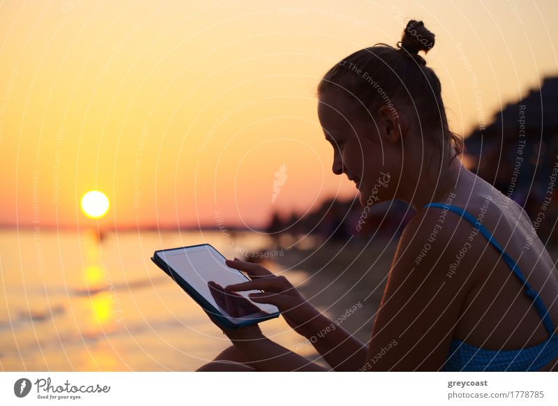 Glückliche junge Frau mit Tablet-PC am Strand bei Sonnenuntergang. Abendsonne, Meer und Strand auf dem Hintergrund Ferien & Urlaub & Reisen Sommer Computer