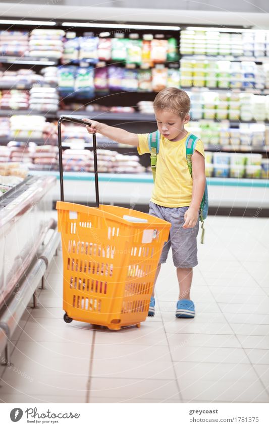Kleiner Junge im Supermarkt schaut auf großen vollen Einkaufswagen. Kind geht allein einkaufen Mensch 1 3-8 Jahre Kindheit blond klein Einsamkeit