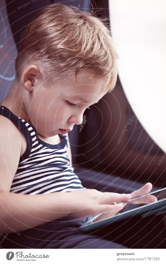 Kleiner Junge sitzt am Fenster im Bus und benutzt das Touchpad, um sich während der Fahrt zu unterhalten Freude Freizeit & Hobby Spielen